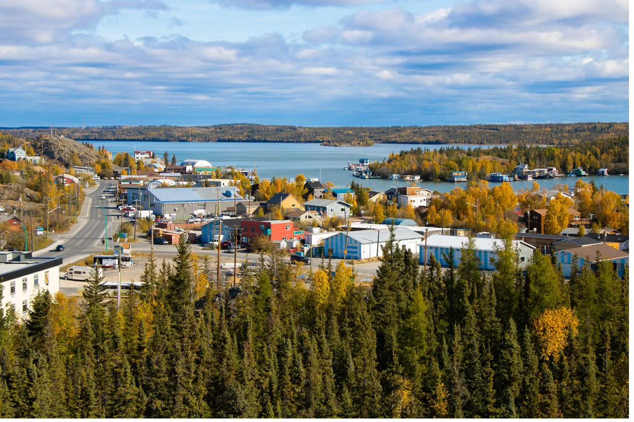 Aerial view of Canadian Indigenous community housing cluster surrounded by boreal forest showing wildfire interface risk