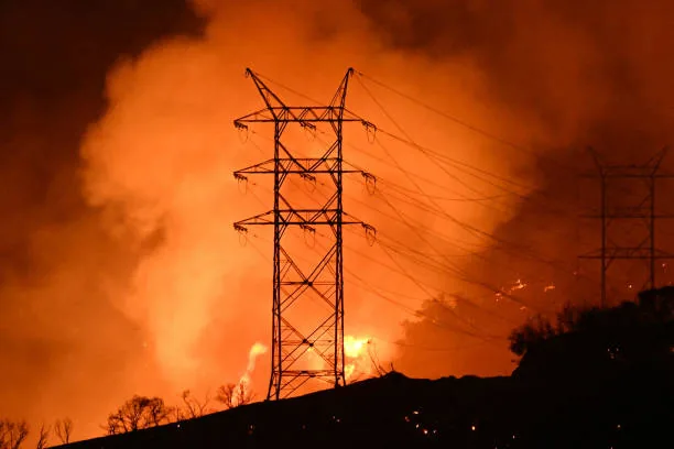 Power transmission tower surrounded by wildfire smoke and orange glow